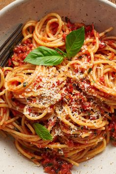 a bowl filled with pasta and sauce on top of a wooden table next to a fork