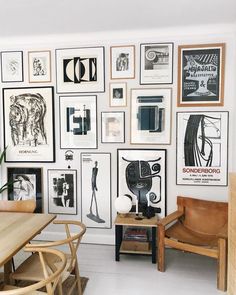 a room filled with lots of framed pictures and art hanging on the wall next to a wooden table