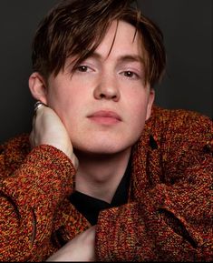 a young man with his hand on his chin looking at the camera while wearing a sweater