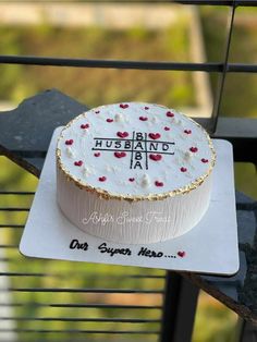 a white cake with red hearts on it sitting on top of a metal table next to a fence