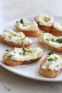 several pieces of bread with cream cheese and herbs on them sitting on a white plate