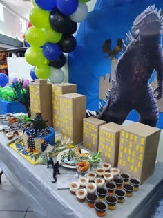 a table topped with cupcakes and cakes next to a giant godzilla balloon in the background