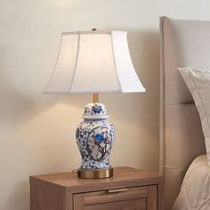 a blue and white vase sitting on top of a night stand next to a lamp