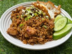 a white plate topped with rice and meat next to cucumbers on the grass