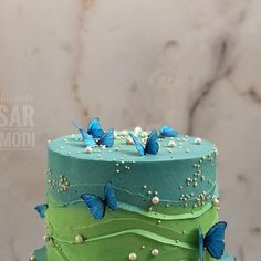 a three layer green cake with blue butterflies on top and white pearls around the edges