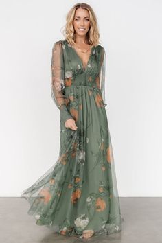 a woman wearing a green floral print long sleeved dress with sheer sleeves and thigh high slit