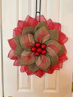 a red and green mesh wreath hanging on the front door with bells attached to it