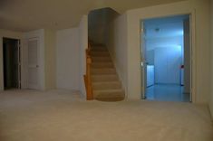 an empty living room with stairs leading up to the second floor and another door in the background