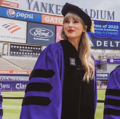 a woman in a graduation gown and cap stands on the field with other people behind her