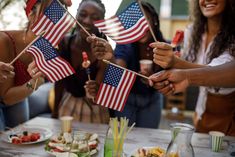 group of people holding american flags on toothpicks in front of food and drinks