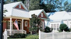 a white picket fence in front of a red house with an american flag on it