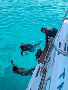 two men are swimming in the water on a boat with another man standing next to them