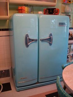 an old fashioned blue refrigerator sitting in a kitchen next to a dining room table and chairs