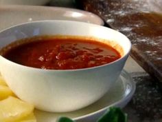 a bowl of tomato soup next to sliced pineapples on a plate with bread in the background