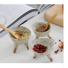 three ceramic bowls with spoons in them sitting on a table next to an open book