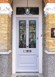 a white front door with stained glass panels on the top and bottom panel, flanked by brick pillars