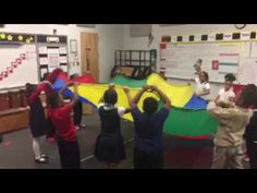 children are playing with a large kite in a classroom