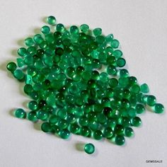 green glass beads are scattered on a white surface