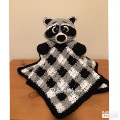 a crocheted raccoon sitting on top of a black and white blanket