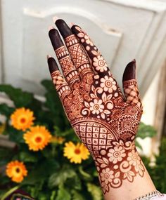 a woman's hand with henna on it and yellow flowers in the background