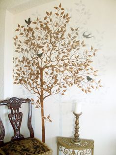 a tree with birds painted on the wall next to a chair and table in front of it