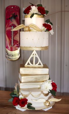 a three tiered cake with white frosting and red flowers on top is sitting on a wooden table