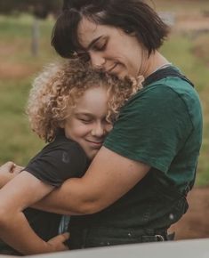 two women hugging each other in front of a fence and green grass covered field behind them