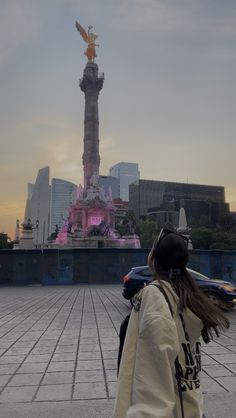 a woman is standing in front of a statue with her hair blowing in the wind