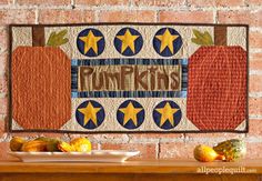 a wall hanging on the side of a brick building with pumpkins and apples in front of it