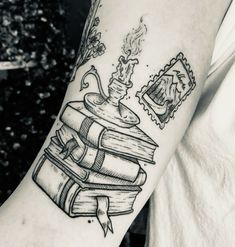 a person with a tattoo on their arm holding a stack of books and an ink lamp