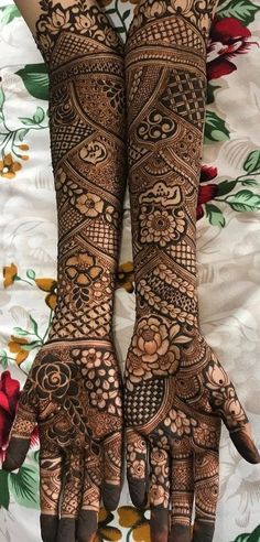 two hands with henna tattoos on them, one is showing the intricate design and the other has flowers