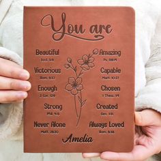 a person holding up a book with the words you are written on it and flowers