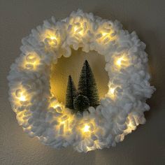 a christmas wreath with lights around it and two small trees in the center, on a wall