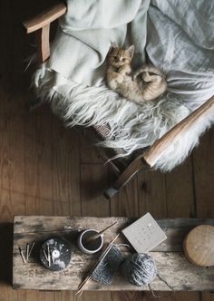 a cat laying on top of a wooden chair next to yarn and knitting needles in a basket