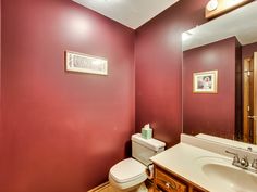 a bathroom with red walls and white fixtures, including a sink, toilet and mirror