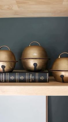 three pots and pans are sitting on top of a shelf next to a book