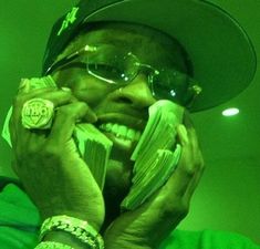 a man in sunglasses and a hat talking on a cell phone while holding money up to his face