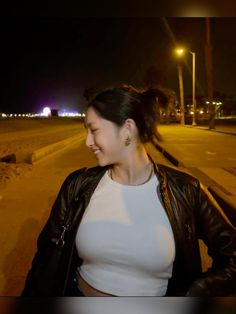 a woman standing on the side of a road at night with her hands in her pockets