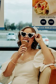 a woman sitting in a chair holding an ice cream cone to her face and wearing sunglasses