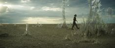 a man walking across a dirt field under a cloudy sky