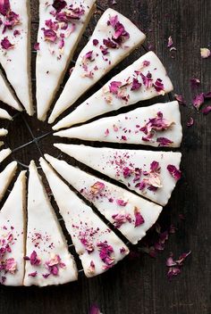 there is a cake with white frosting and pink flowers on the top, surrounded by petals