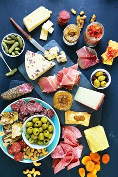 an assortment of cheeses, meats and olives are arranged on a table