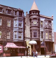 an old photo of some buildings and people on the sidewalk in front of them,