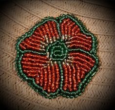 an orange and green beaded flower on a piece of woven material with some beads around it