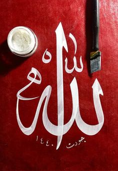 an arabic calligraphy written in white on a red surface next to a black brush