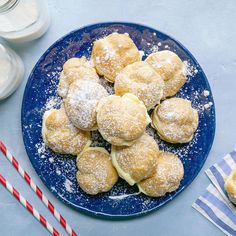 a blue plate topped with powdered sugar covered pastries next to two glasses of milk