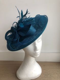 A striking two tone peacock blue coloured fascinator, composed of a circular teal Sinamay base adorned with loops of vibrant peacock blue Sinamay and finished with hand shaped feathers in the same glamorous shade. A striking addition to any formal outfit. Fascinator measuring approx 30cm in diameter. Please note as our fascinators are hand dyed to order if you feel this colour may not be quite right please request to see a colour chart. If you would like the fascinator created in an alternative dye colour which we don't currently stock there will be a charge of £30 to cover the cost of the dye and the labour. Our timeless pieces are perfect for any special occasion from Weddings to The Kentucky Derby and Summer Garden Parties! We offer ready to wear pieces in a variety of styles and colour Elegant Turquoise Fascinator For Races, Elegant Turquoise Fascinator For Kentucky Derby, Elegant Turquoise Fascinator For Wedding, Turquoise Fascinator For Spring Party, Elegant Turquoise Fascinator For Royal Ascot, Fitted Turquoise Hat For Party, Turquoise Fitted Hat For Party, Turquoise Fitted Party Hat, Turquoise Spring Party Fascinator