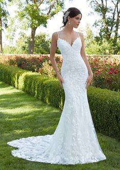 a woman in a white wedding dress standing on the grass with her hands behind her back