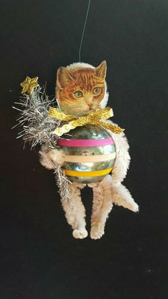 a cat that is hanging from a christmas ornament with tinsel on it