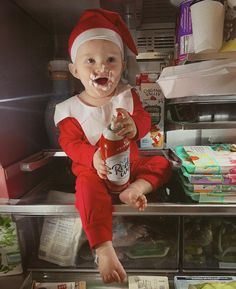 a baby dressed as santa clause holding a bottle of ketchup